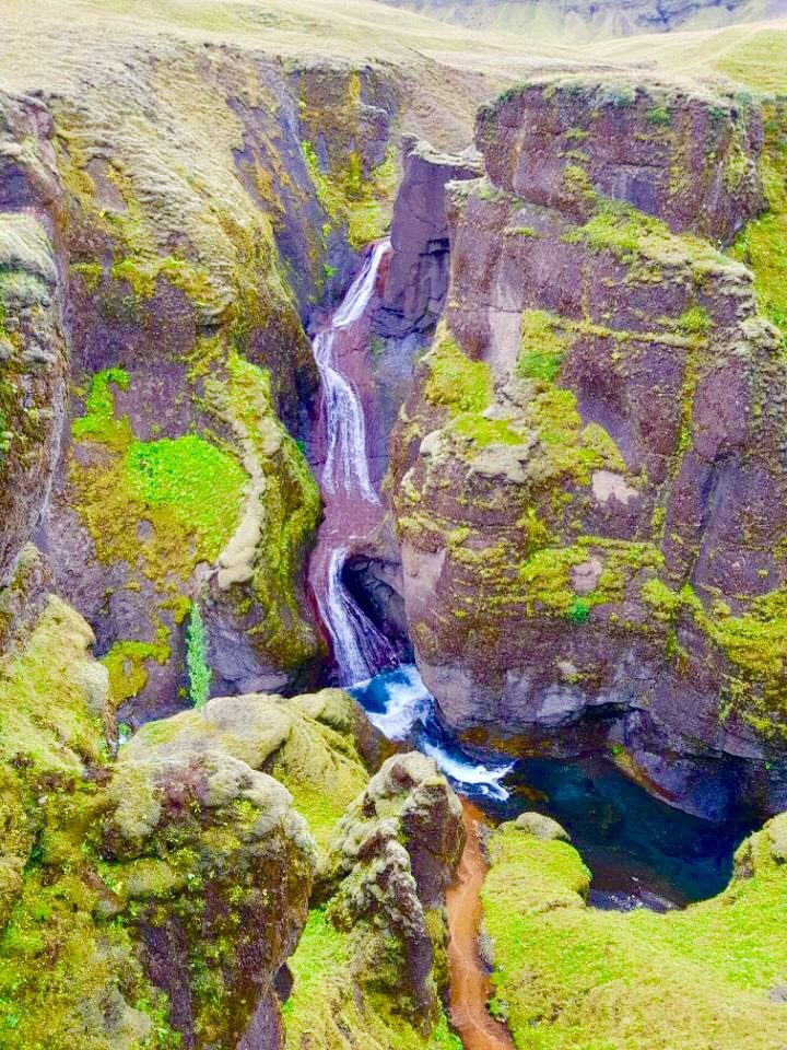 A narrow waterfall cutting through a green gorge