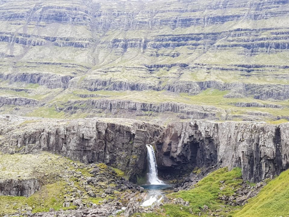 A small waterfall at the base of striated mountain layers